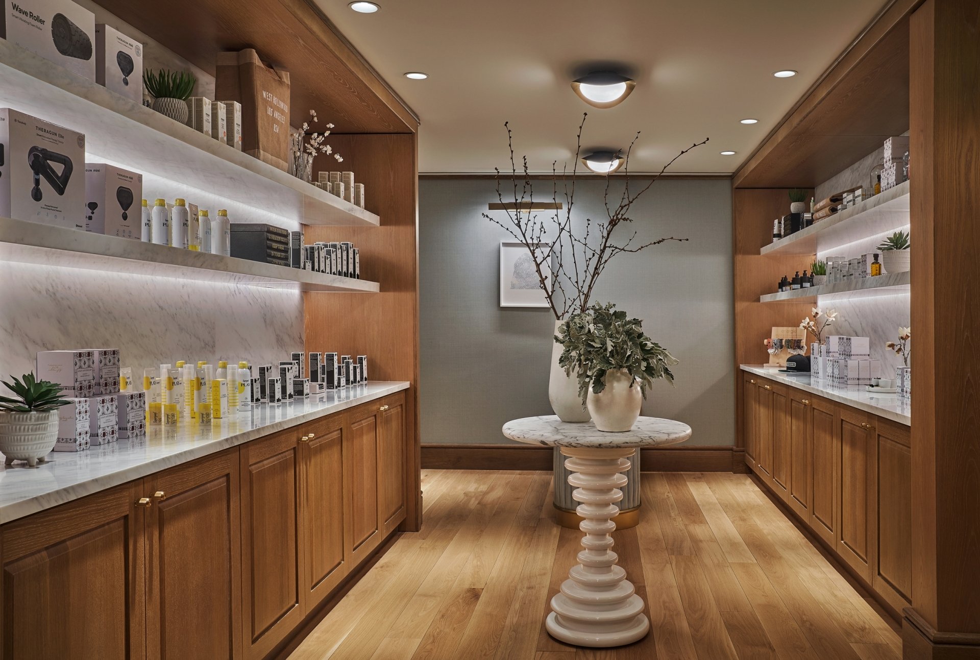 A spa retail room with wood shelving, marble counters, and a central scalloped table decorated with branches and greenery.