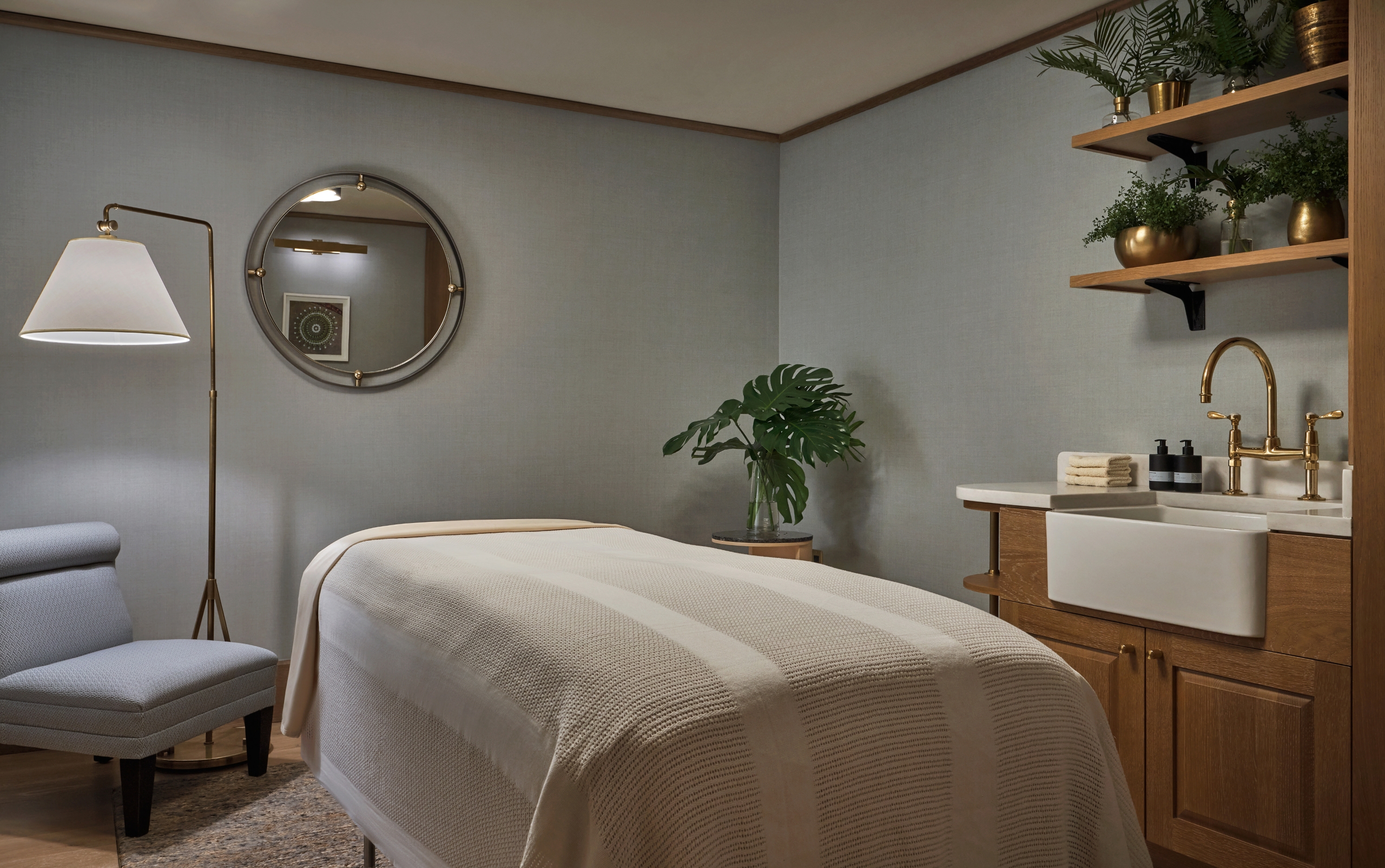 A massage table in the spa at The Sun Rose, with a lamp, mirror, sink, and greenery around it