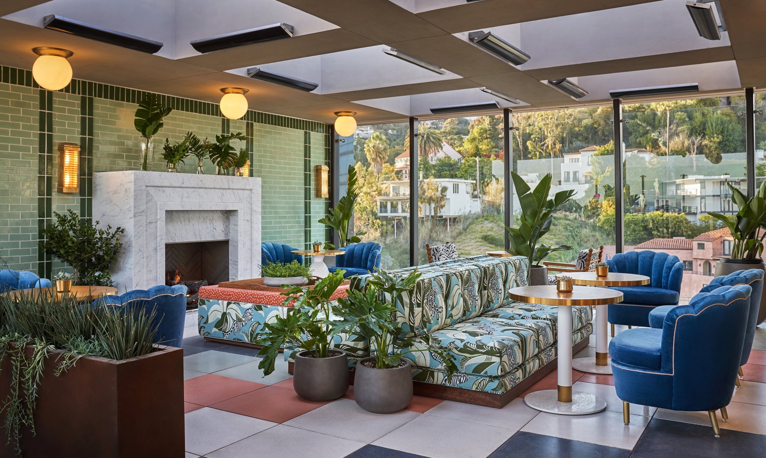 The Bar At Merois dining area with large couches, tables & chairs with a large fire place and views of West Hollywood in the background