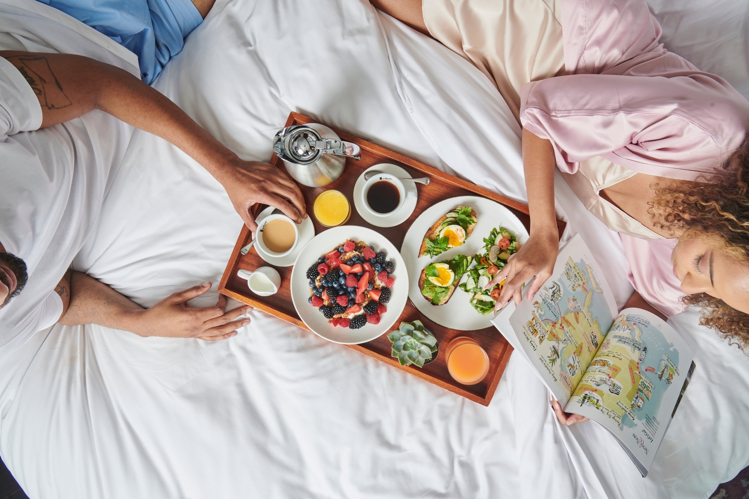 A couple laying in bed enjoying their freshly prepared breakfast at The Sun Rose