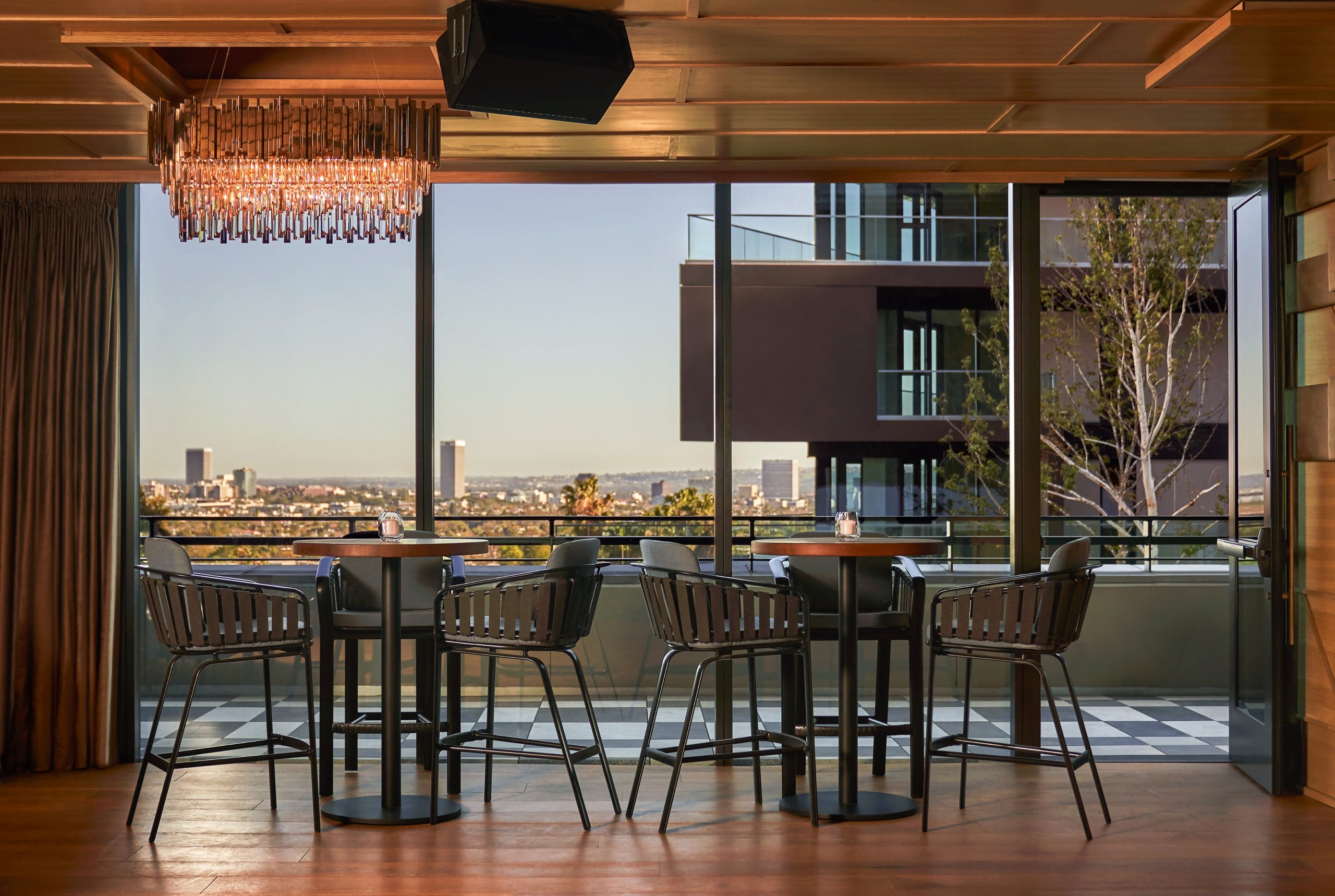 Two tables with chairs in front of a large window section with views of West Hollywood in the background