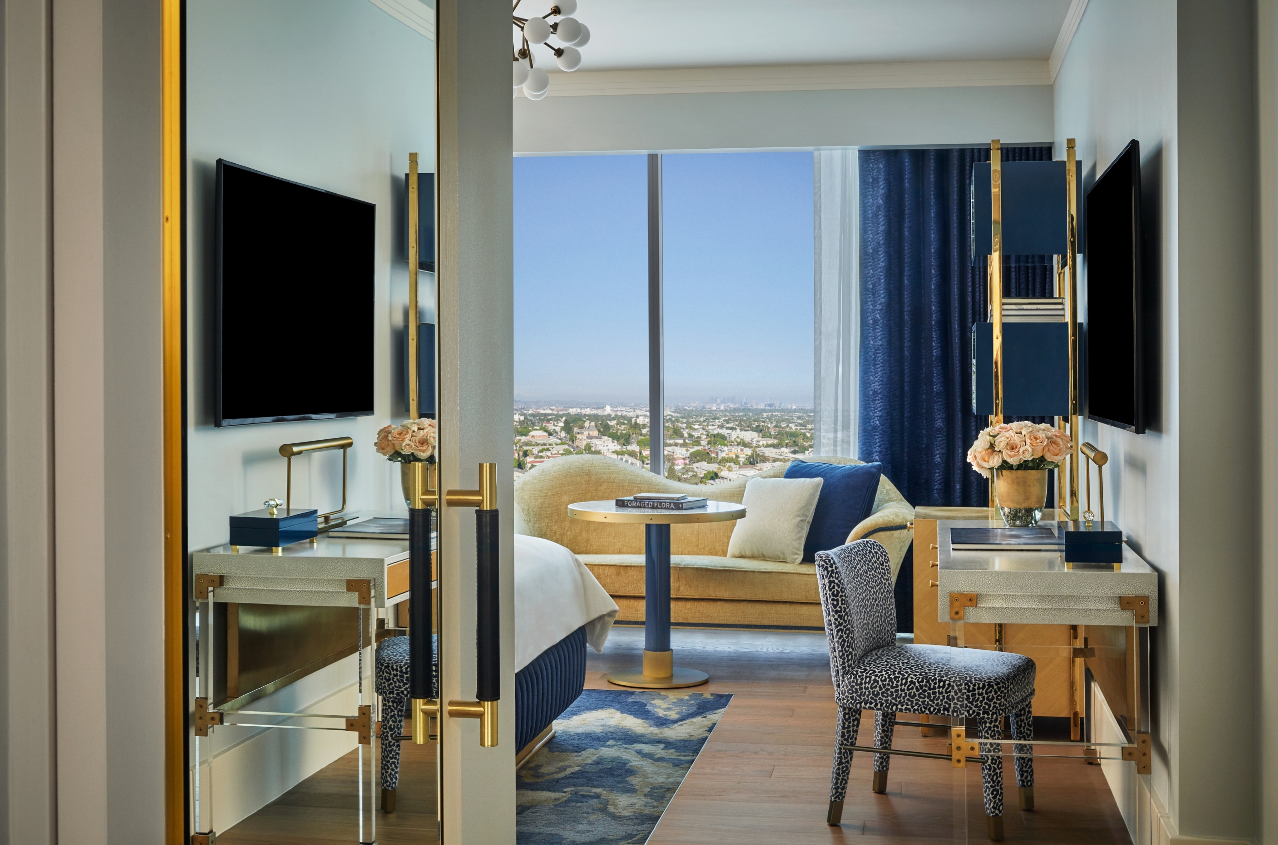 An interior view of a room at The Sun Rose with a desk and chair, large couch and views of West Hollywood in the background