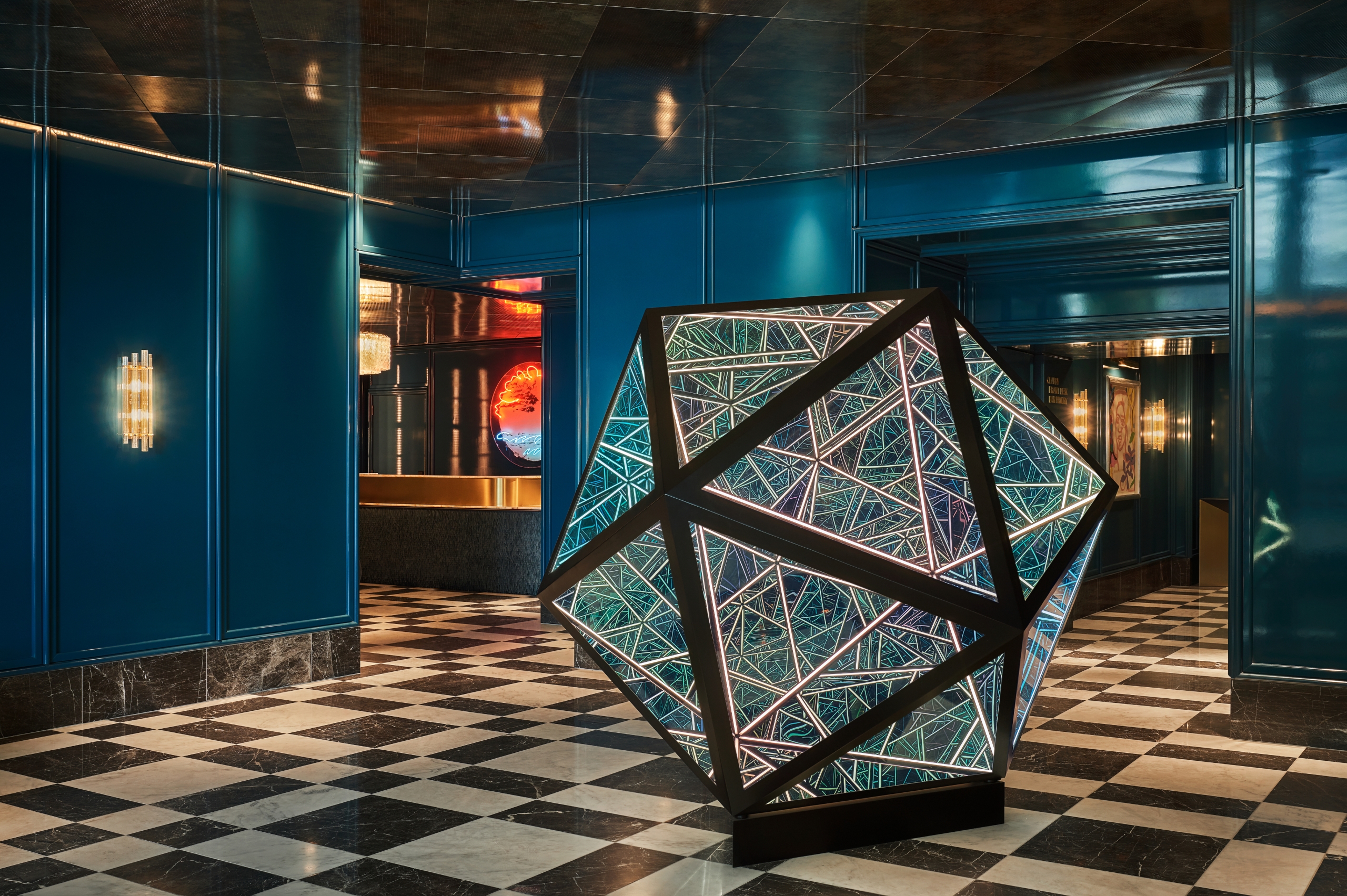 icosahedron by anthony james,. a large illuminated geometric art sculpture, sits on a black and white checkered floor in a luxe and modern hotel lobby in West Hollywood.
