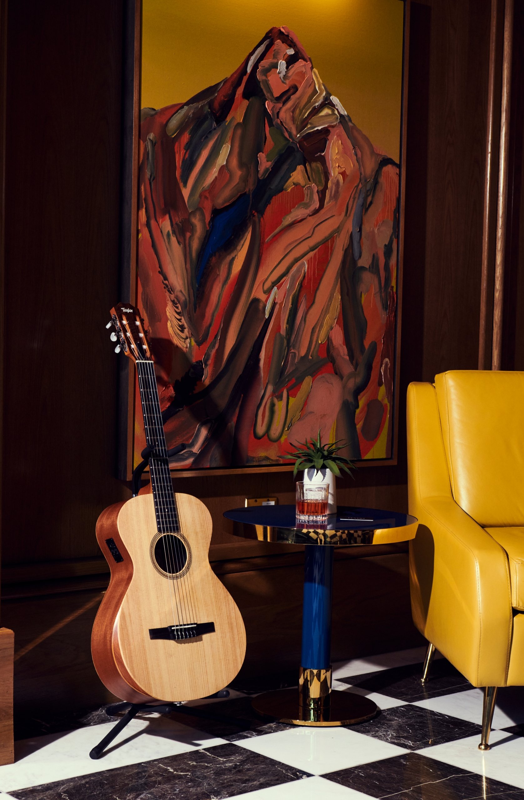 A close up of a guitar sitting next to a table in front of a abstract art piece at The Sun Rose