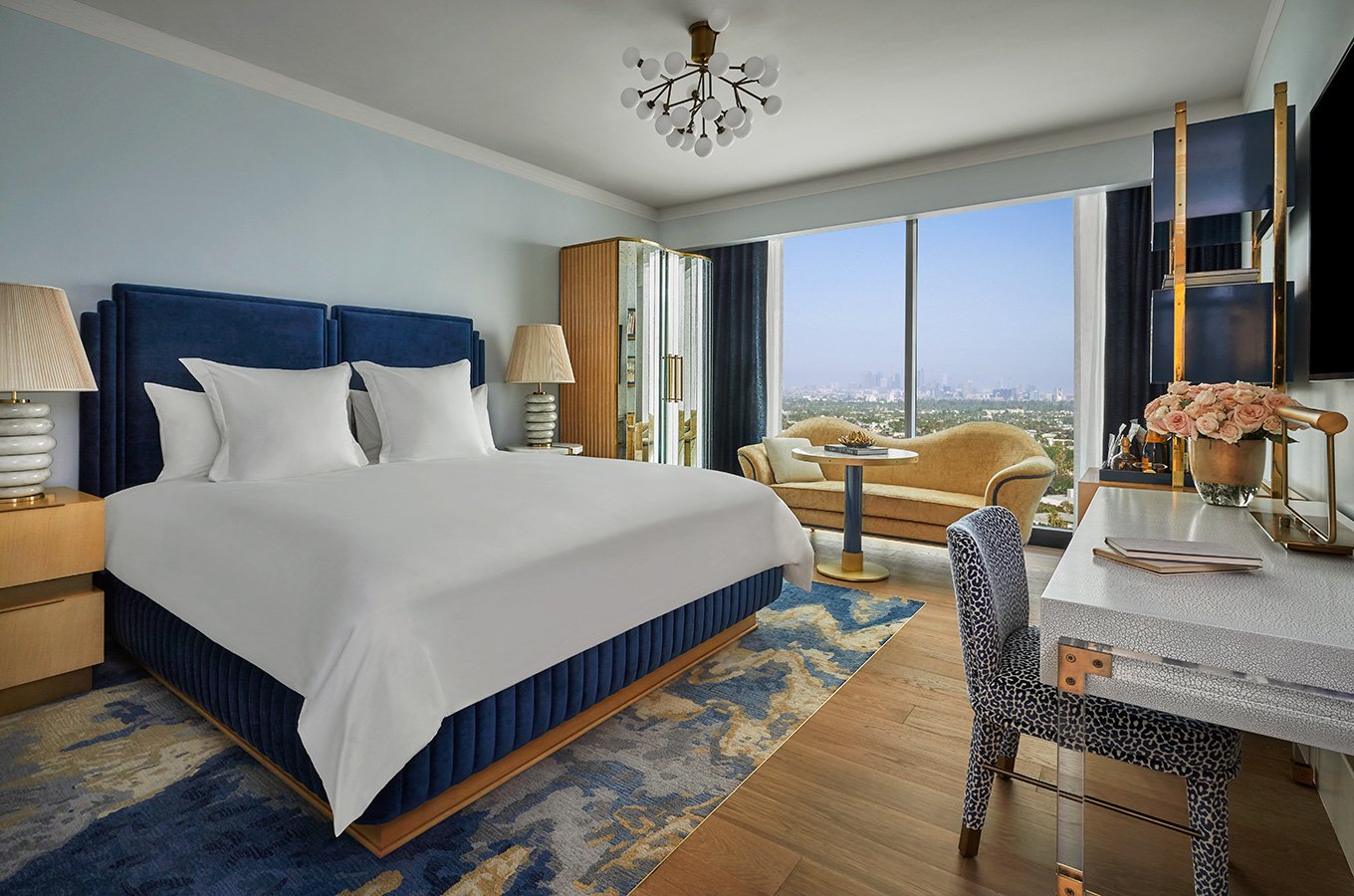 An interior view of a room at The Sun Rose with a large bed, working desk and couch along with views of West Hollywood in the background