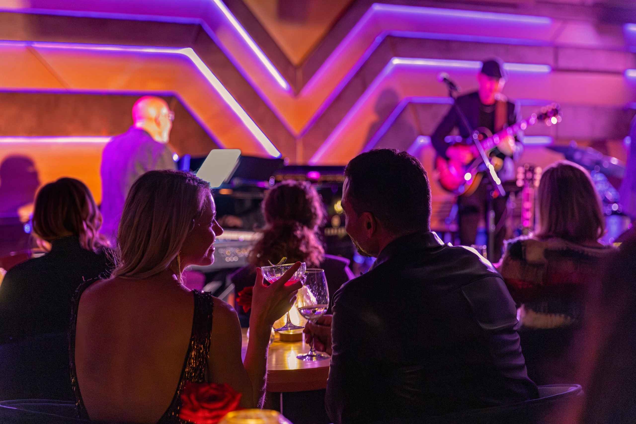 A woman in a sequined dress toasts with a cocktail while enjoying live music in an intimate, upscale jazz club.