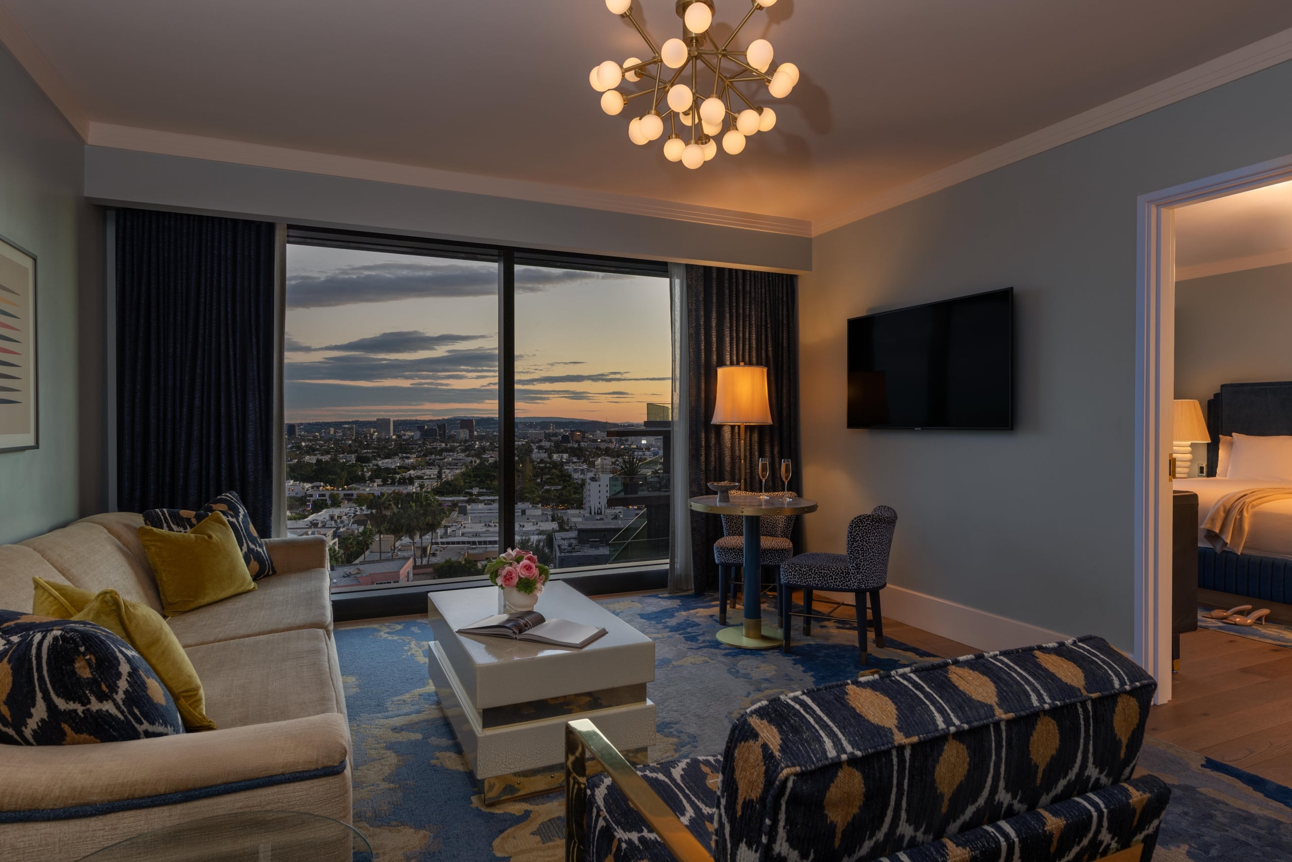 A modern hotel suite living room with a navy patterned sofa and a large window facing the city.