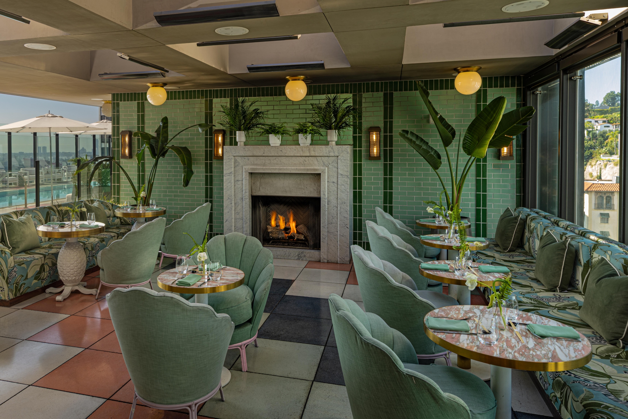 A sophisticated dining area at The Sun Rose featuring floral banquettes, green velvet chairs, and a warm fireplace.