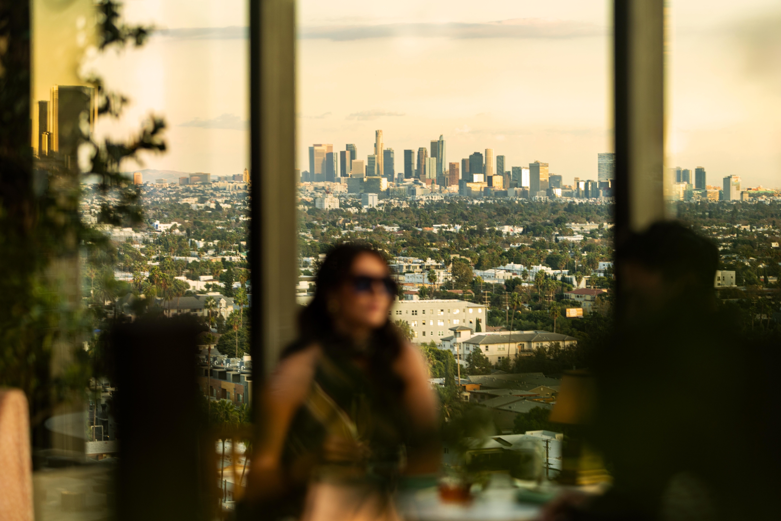 A soft-focus view of a couple dining on a terrace, highlighting a sharp, clear view of distant downtown skyscrapers.