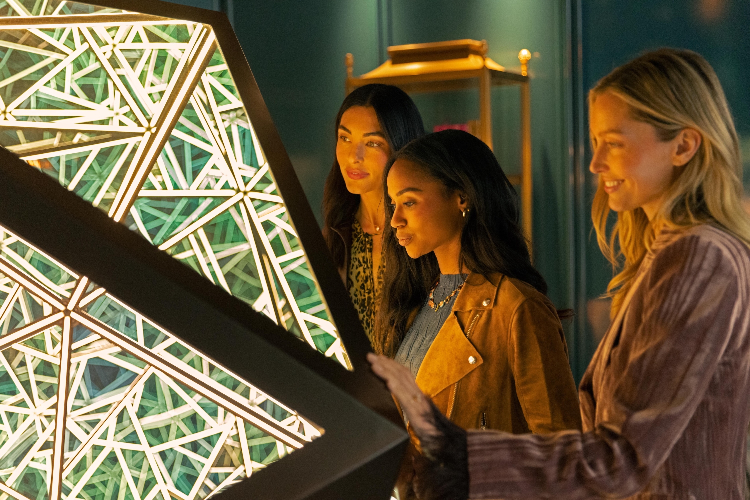 A close-up of three friends admiring a modern, geometric light installation inside the moody, chic lounge of The Sun Rose.