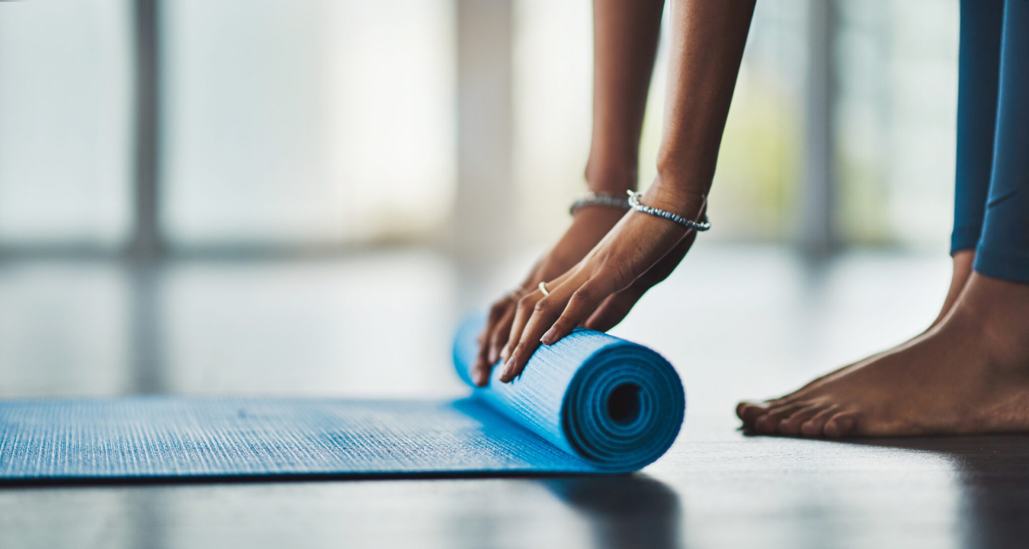 woman rolling up a blue yoga mat on the ground