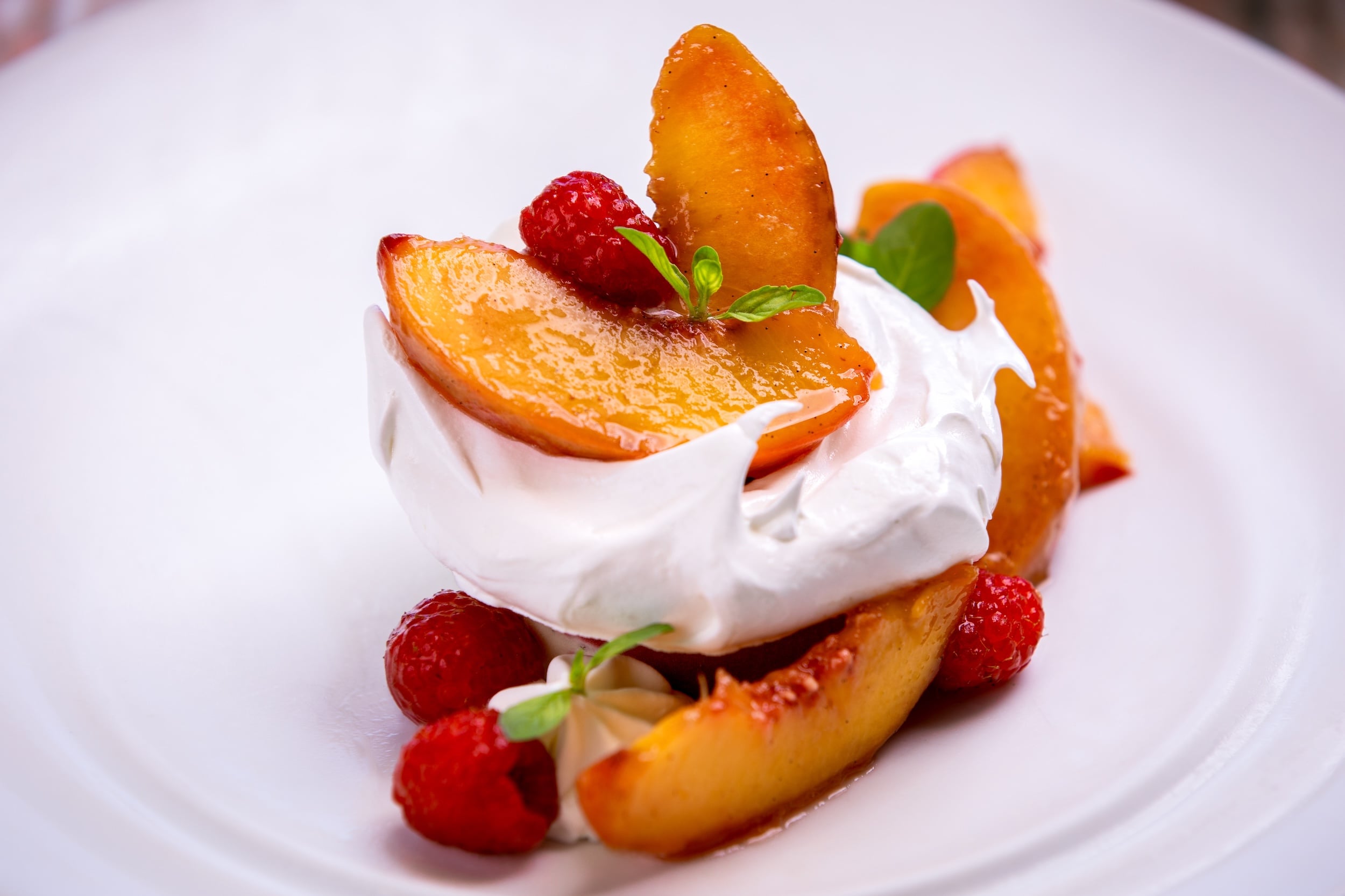 A plated peach melba pavolova dish.